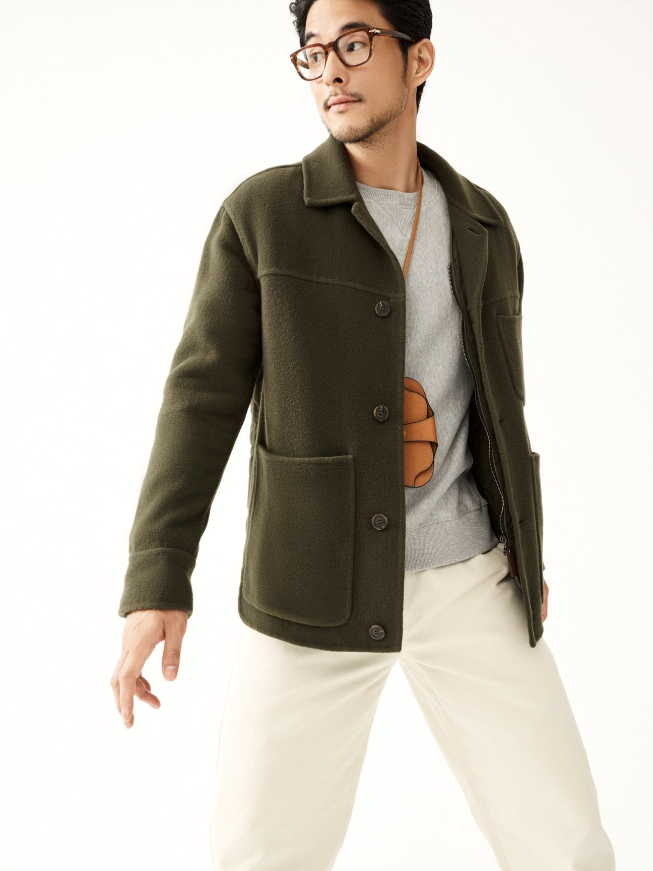 Man in olive green wool jacket and beige trousers looking upward against white background