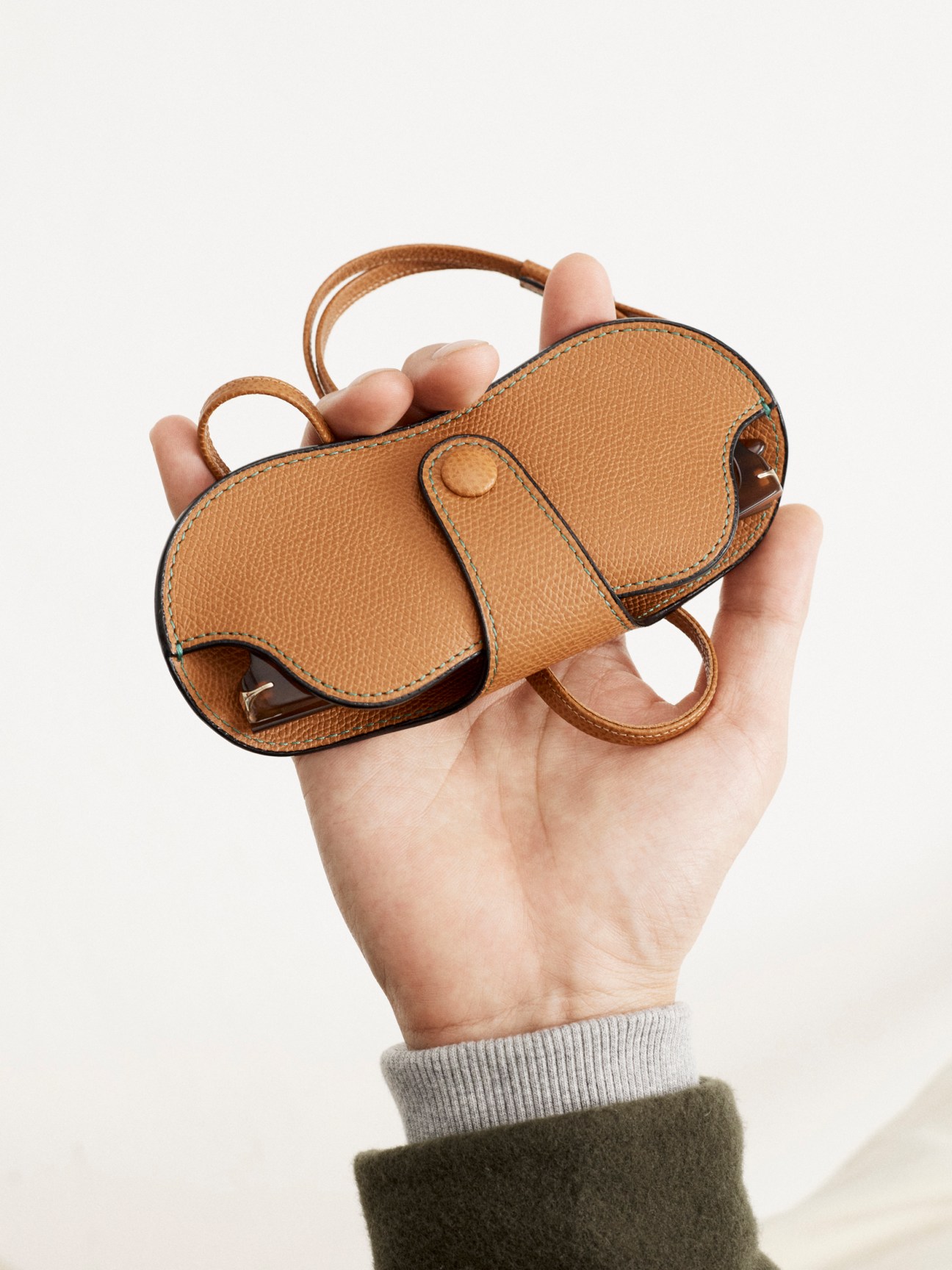 Hand holding a small tan leather elephant-shaped glasses case with handles against a light background