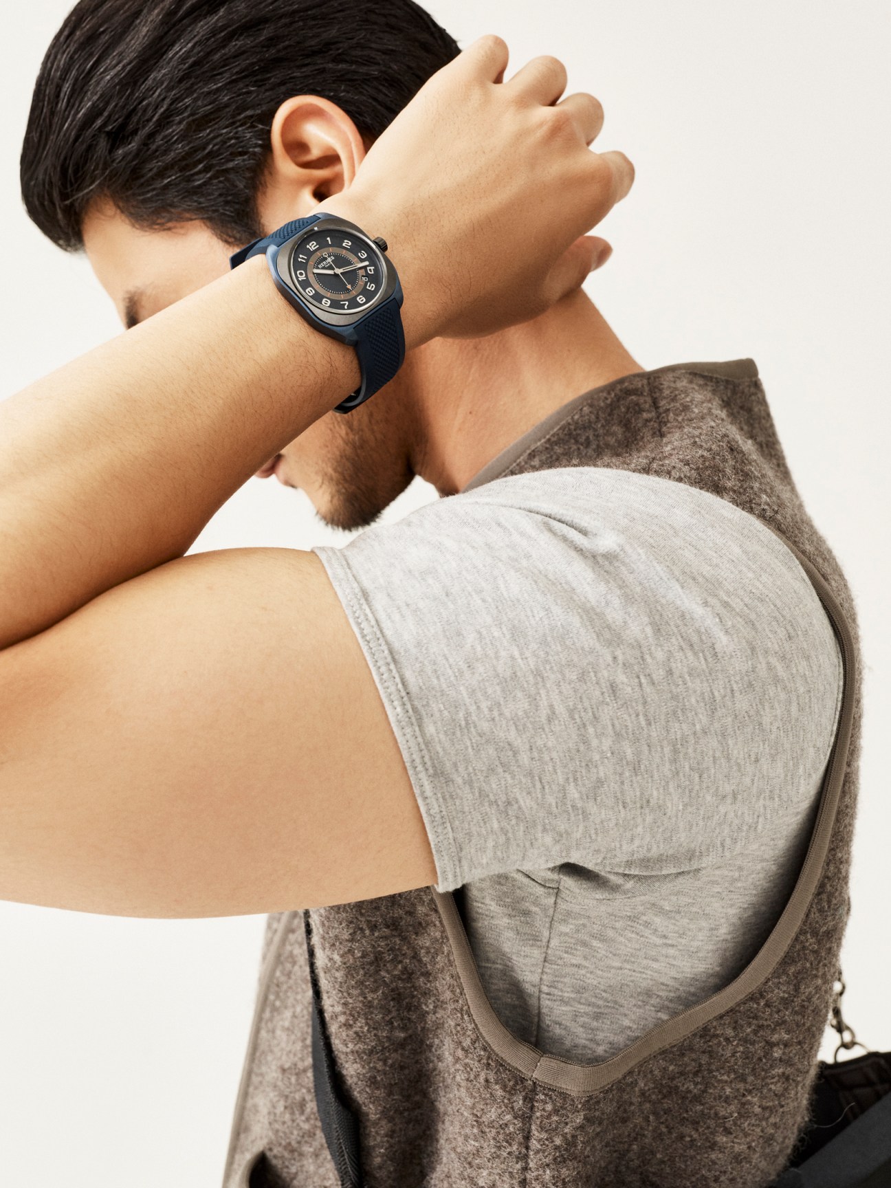 Man wearing grey hoodie and blue Hermès H08 Chronograph watch with hand positioned behind head