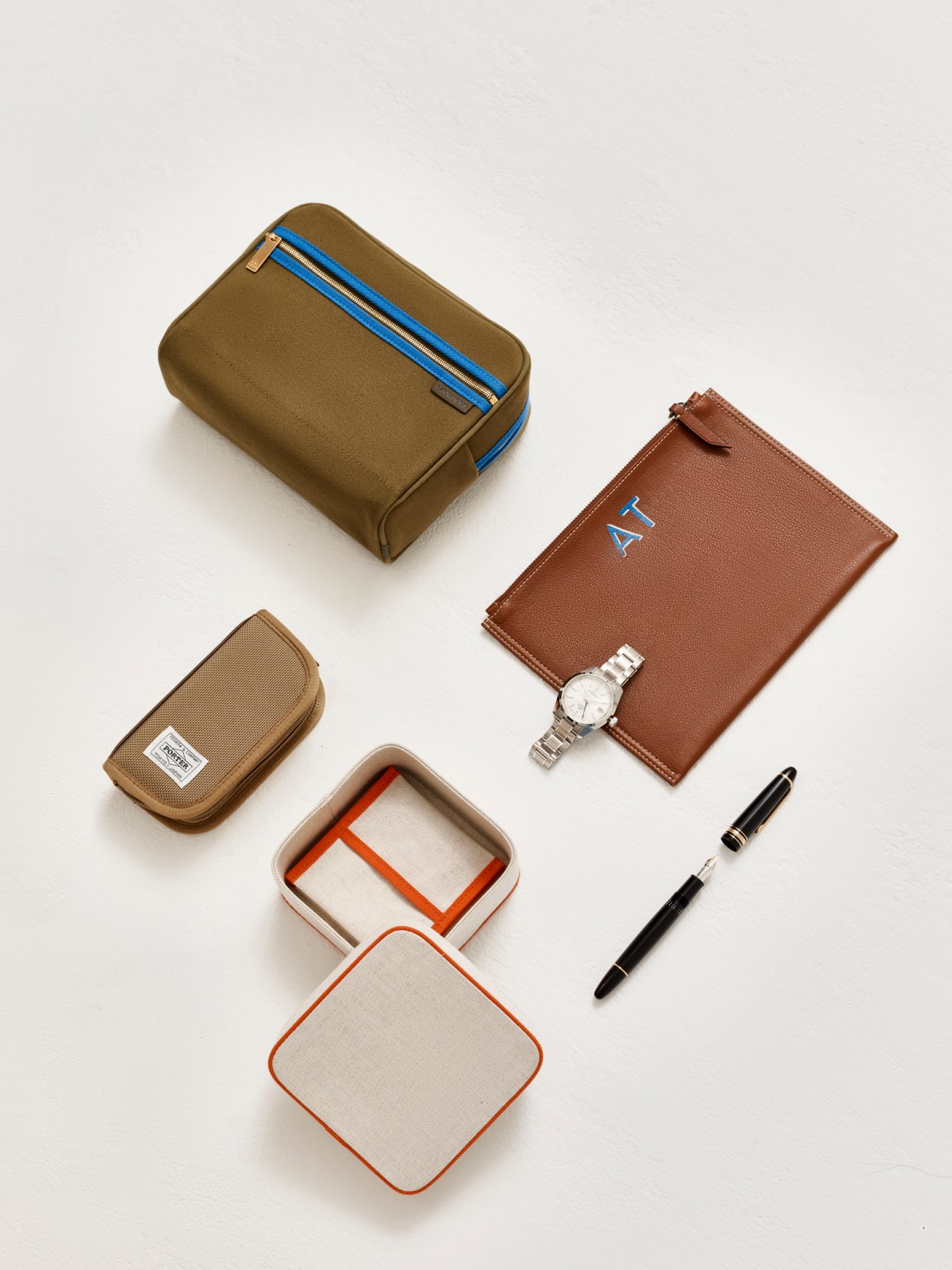Flat lay of men's accessories including leather wallets, watch, pen, and storage cases in brown and beige tones