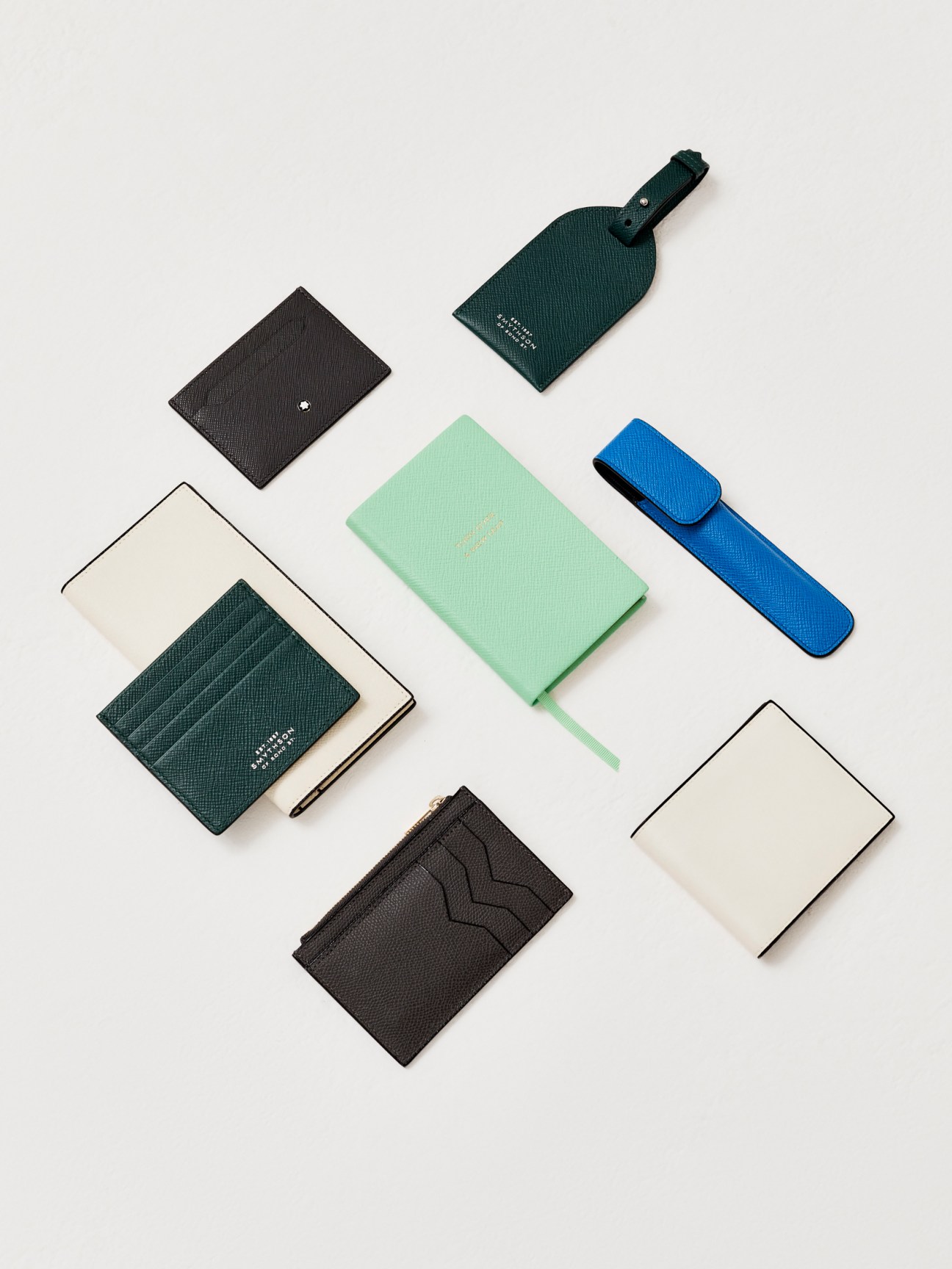 Various leather accessories in green, black, white and blue arranged on white background including wallets, tags and cases