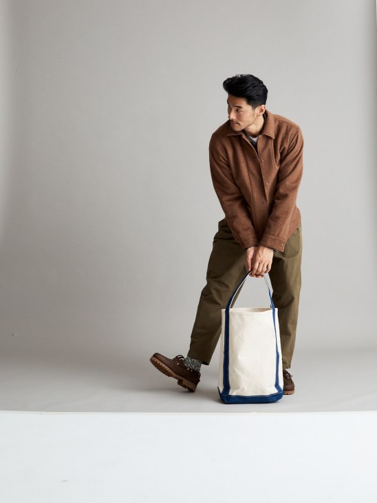 Model in casual layered look with jacket, shirt and bag in natural setting