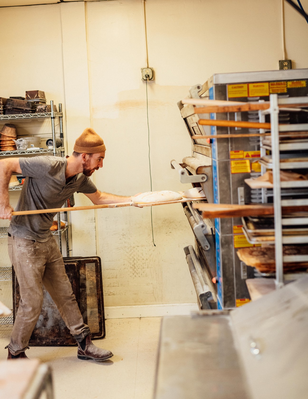 Baker Aaron Hall removes a loaf of sourdough bread from an oven in his bakery.