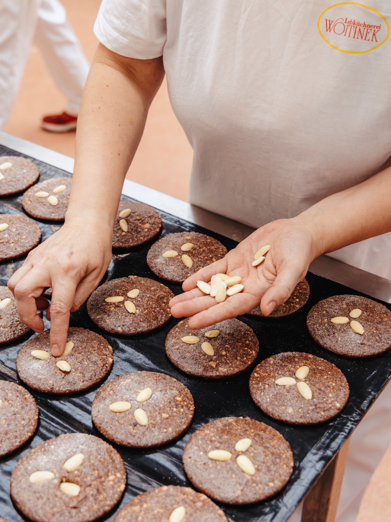 Hands decorating round gingerbread cakes with almond slivers at Lebküchnerei Woitinek in Nuremberg.