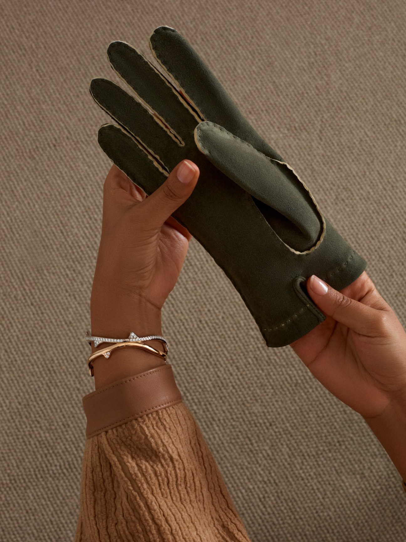 Hands holding black leather gloves with bracelets visible on the wrist.