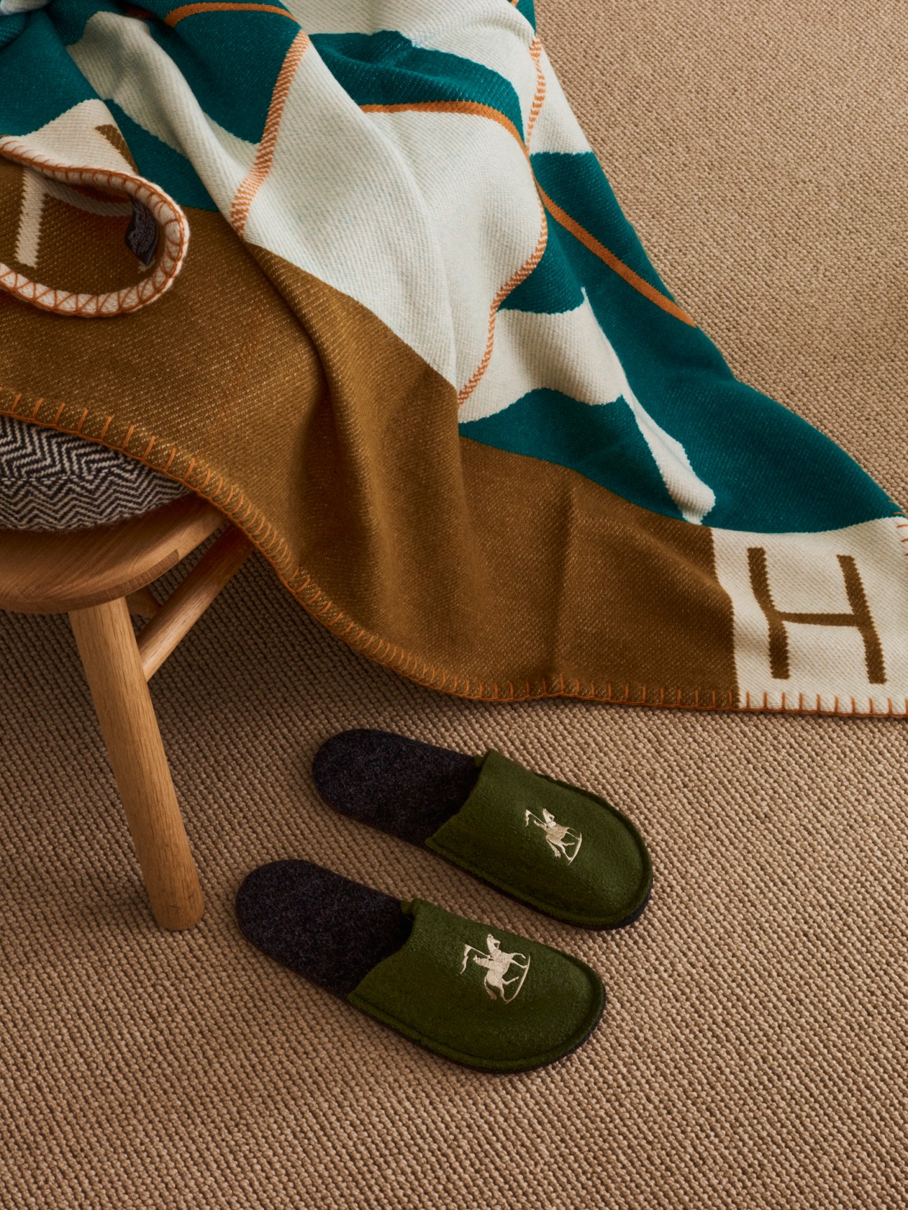 Hermès blanket with teal, white and orange geometric pattern draped over wooden chair with Ludwig Reiter slippers on floor.