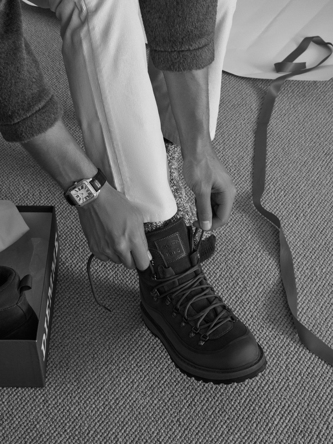 Person lacing Diemme 3 Ten C boots while wearing Hansen jacket, Trunk trousers, and Cartier Santos-Dumont watch.