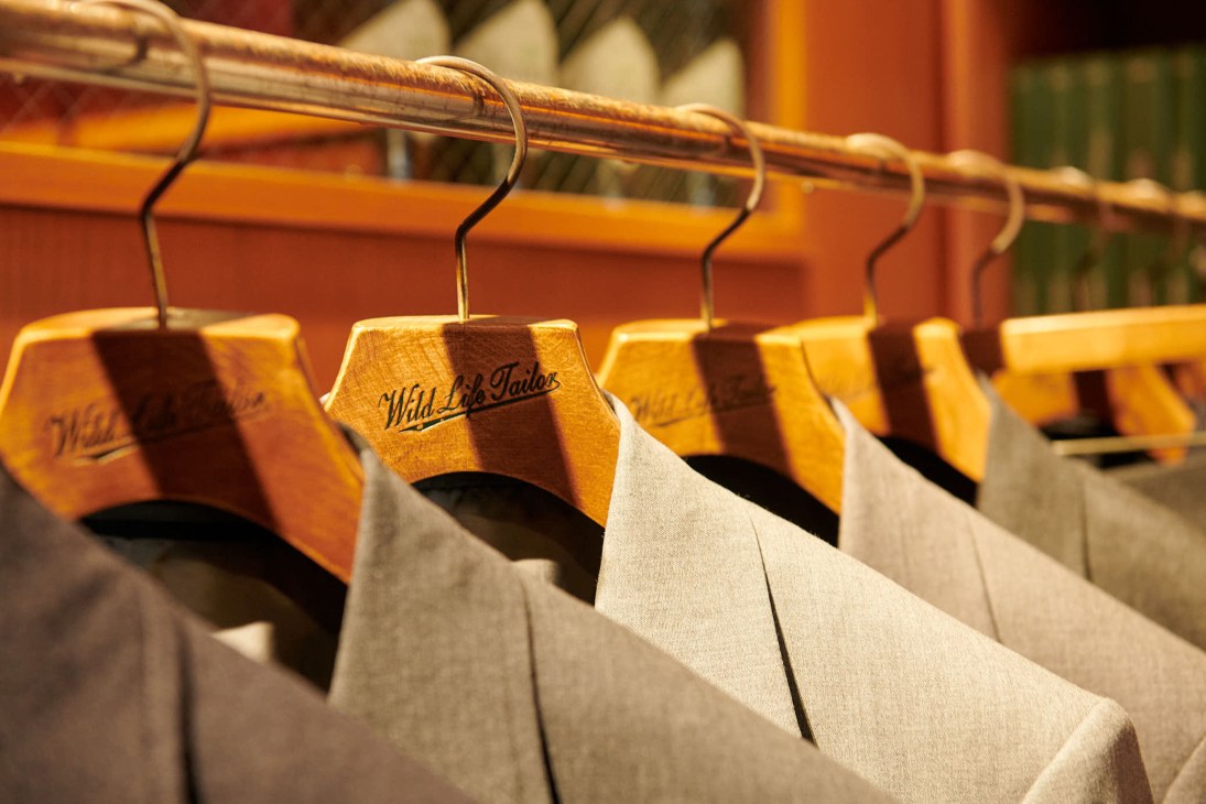 Wild Life Tailor custom suits hanging on wooden hangers with the brand's striped logo in a Tokyo shop.