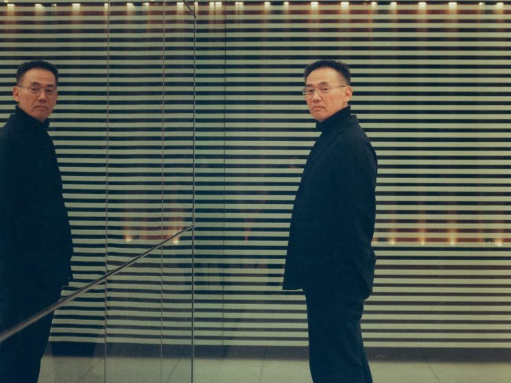 Susumu Sasaki in dark clothing standing next to mirrored wall with horizontal striped pattern