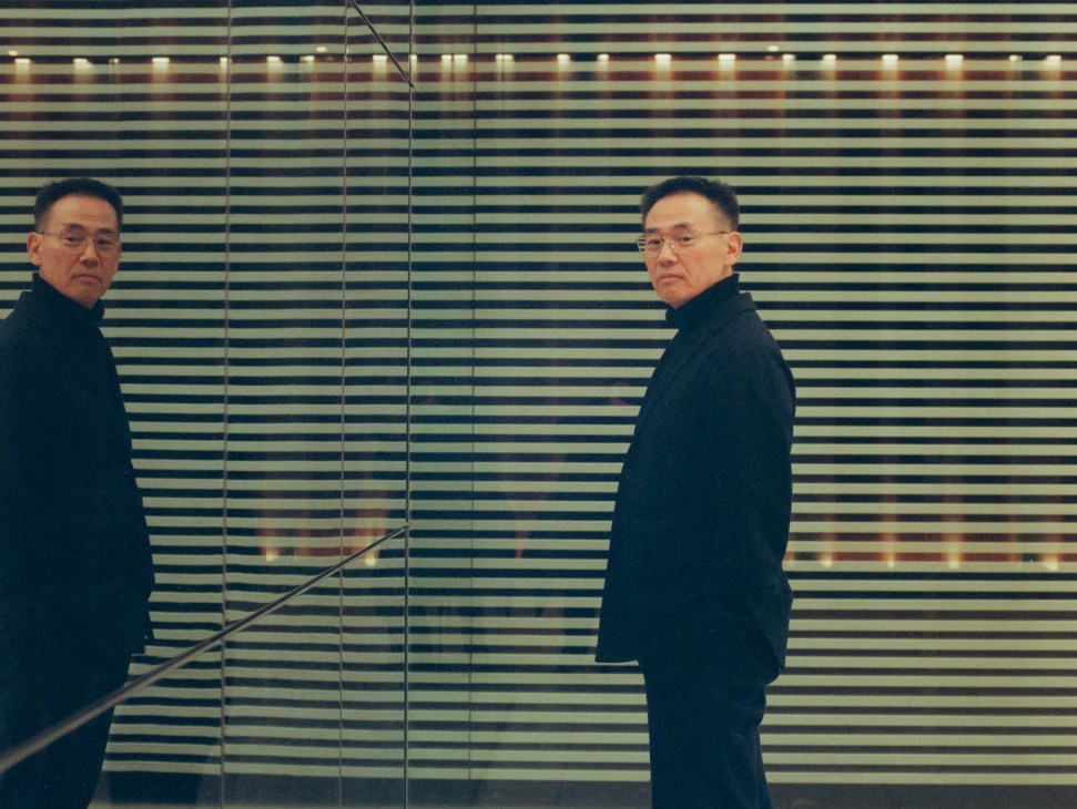 Susumu Sasaki in dark clothing standing next to mirrored wall with horizontal striped pattern