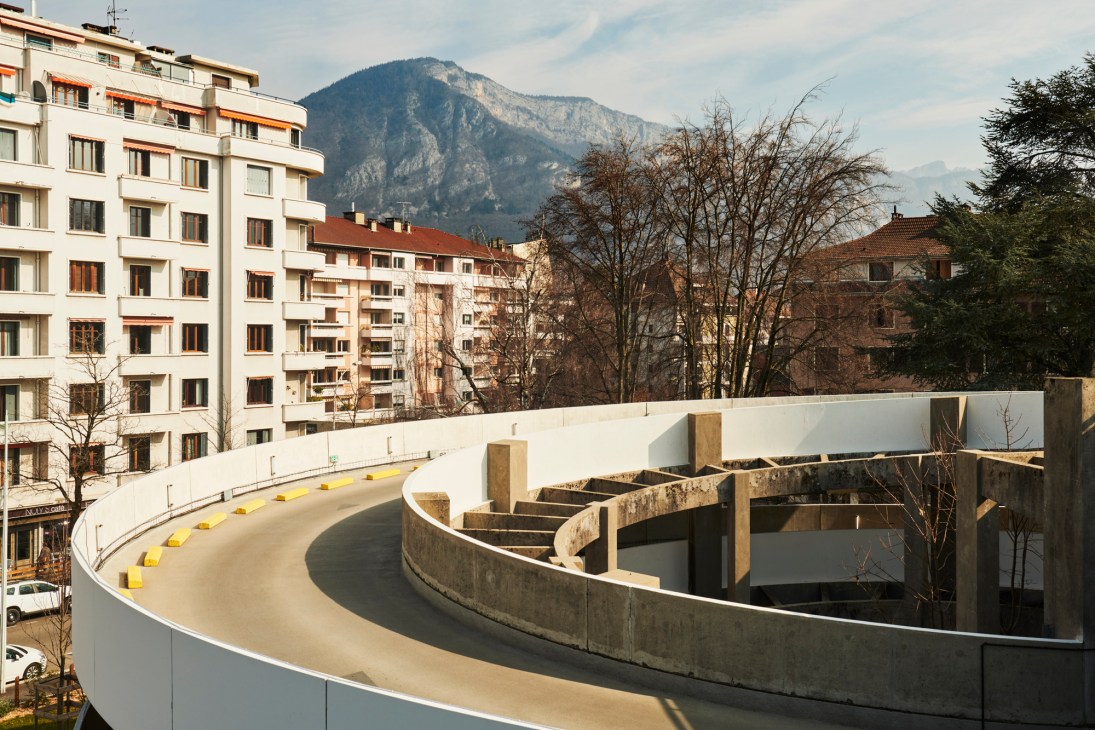 Curved concrete parking ramp with mountain backdrop and apartment buildings in Alpine city