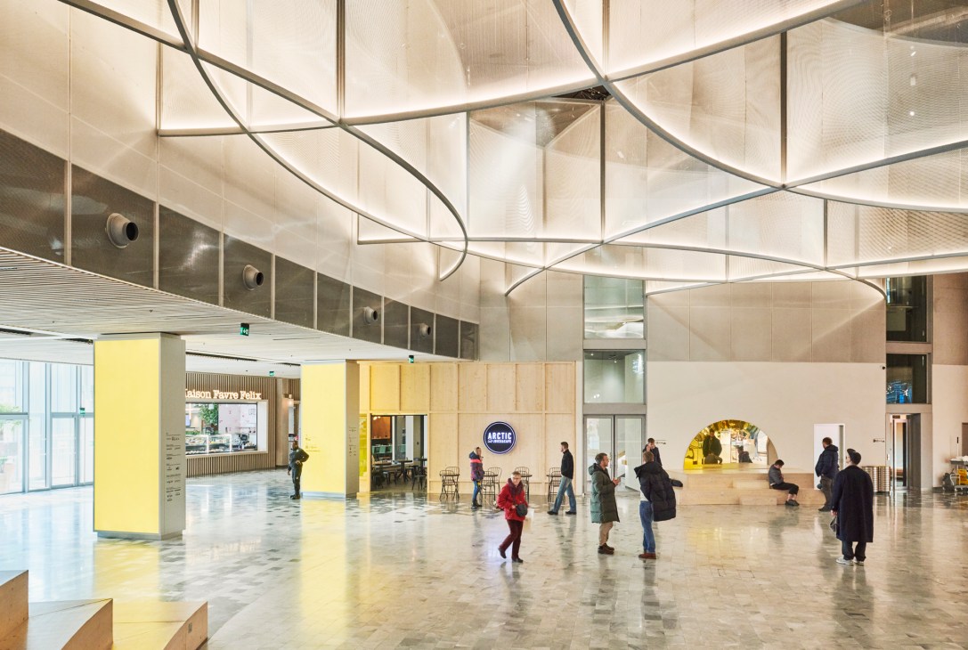 Modern interior with curved metal sculptural installation overhead and people walking through bright open space