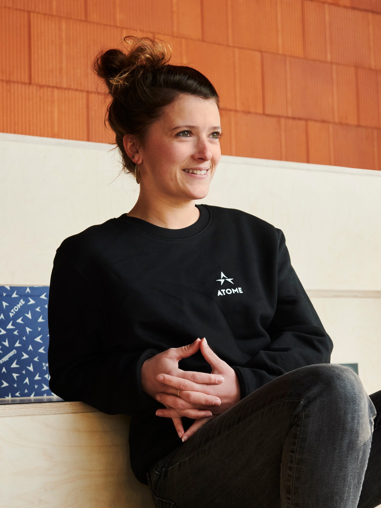 Helena Celestini, manager of Atome climbing gym, sitting on white couch wearing black Atome sweatshirt