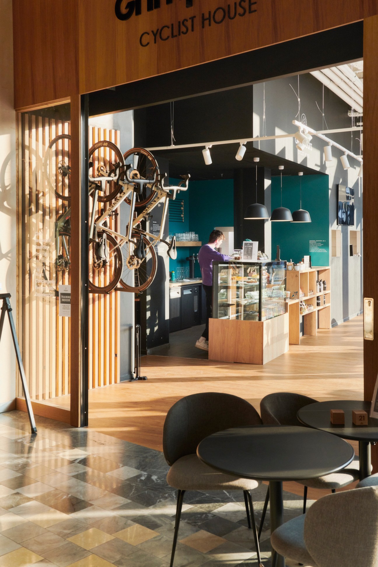 Interior of cyclist shop showing bicycle hanging from ceiling, display cases, and person in purple shirt