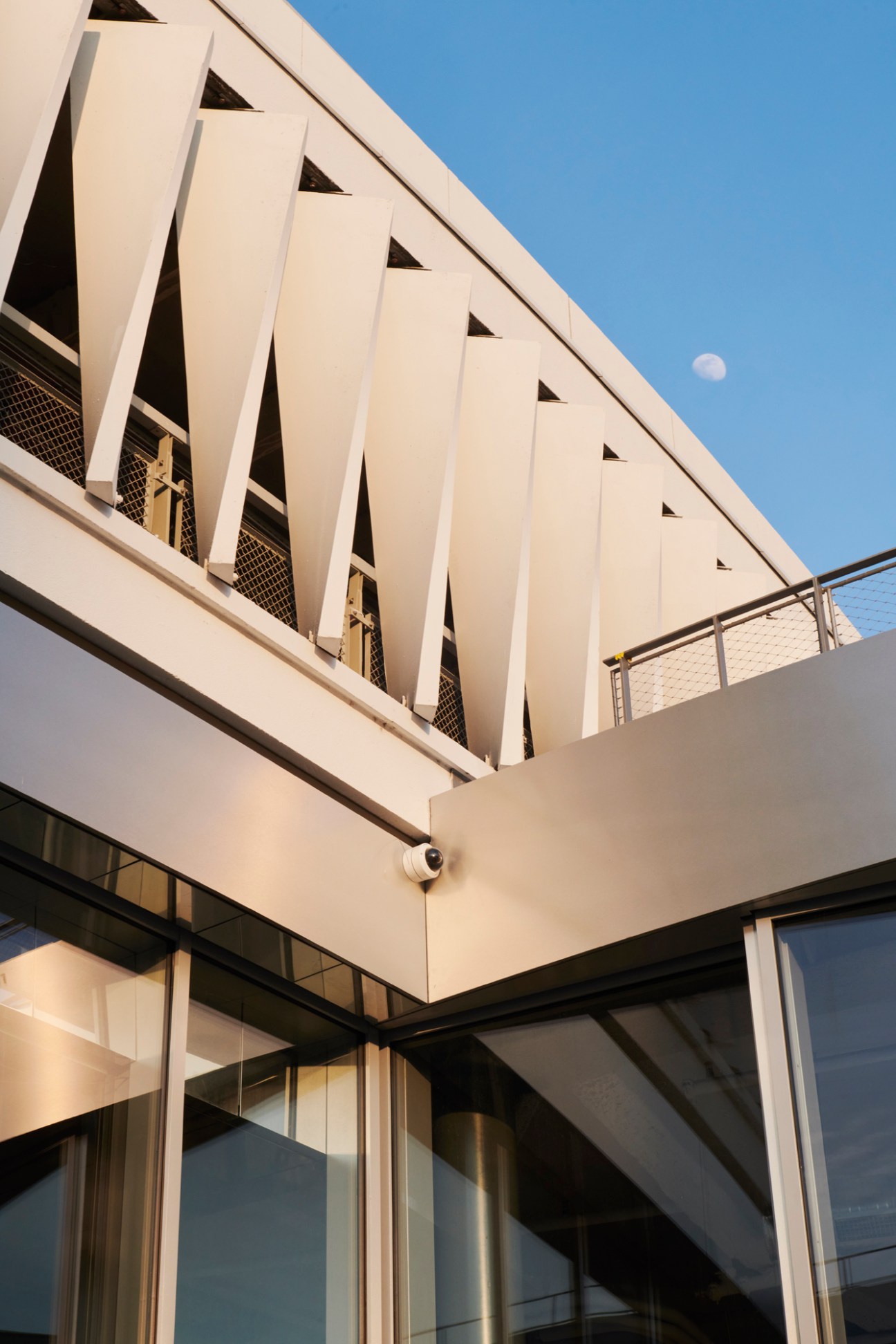 Modern glass storefront with curved architecture next to white concrete building under blue sky with moon visible