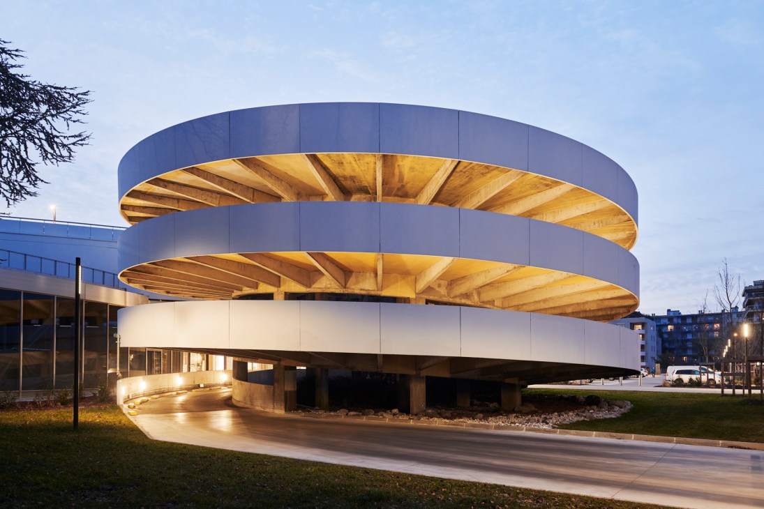 Modern circular building with illuminated wooden ceiling overhangs and concrete structure at twilight