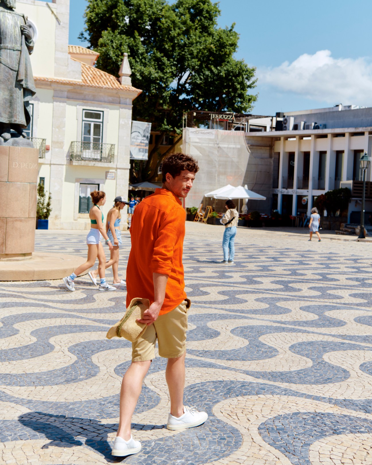 Man in orange shirt and beige shorts walking on decorative cobblestone plaza in Lisbon
