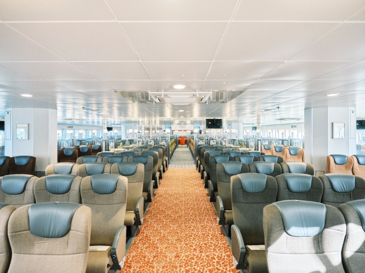 Interior view of Queen Beetle ferry's standard class passenger seating area with blue and gray chairs