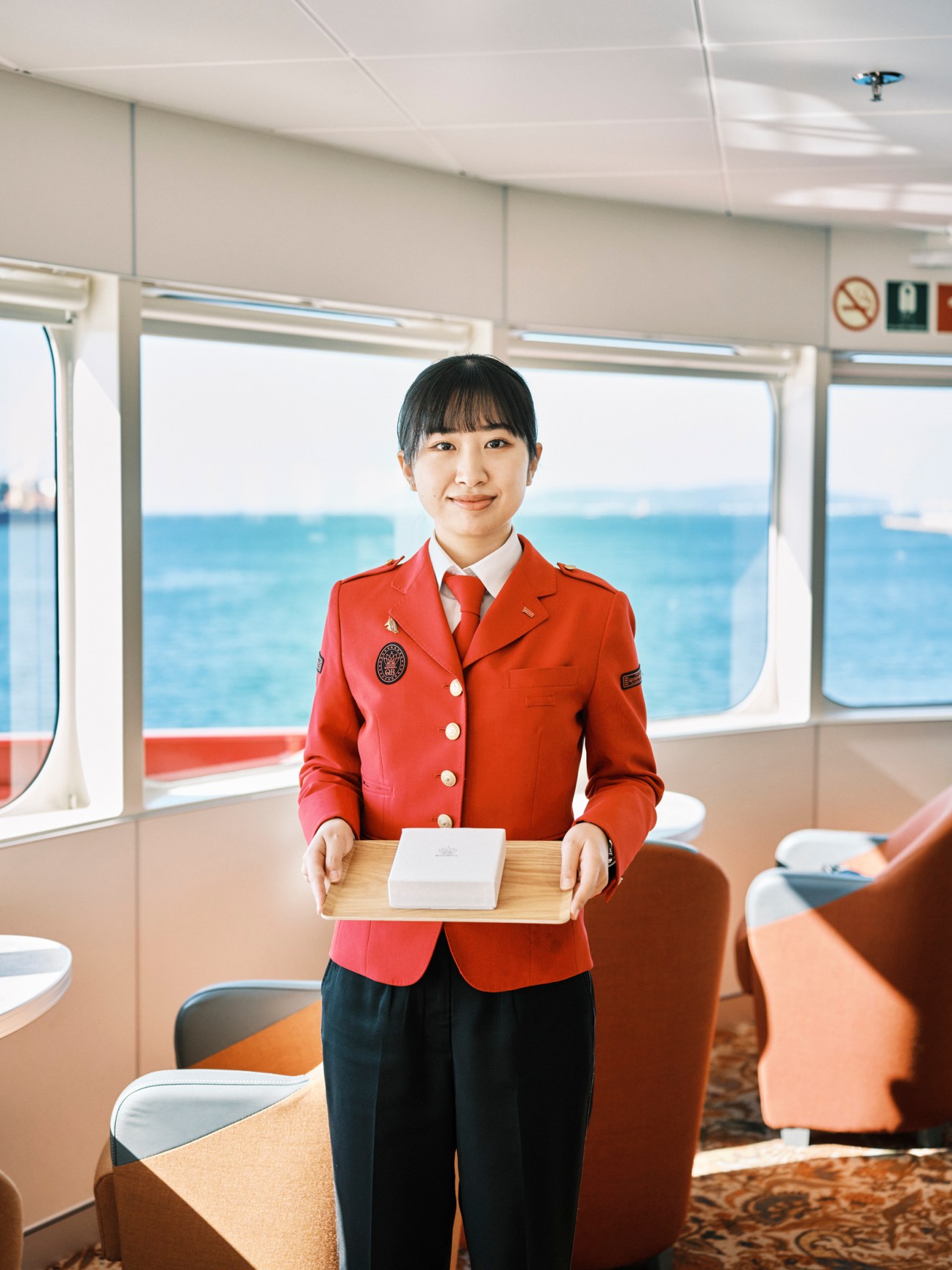 Ferry crew member in red uniform holding wooden tray aboard Queen Beetle ferry