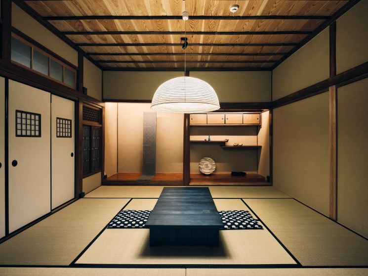 Traditional Japanese room with tatami floors, exposed wooden beams, paper lantern, low table and built-in shelving