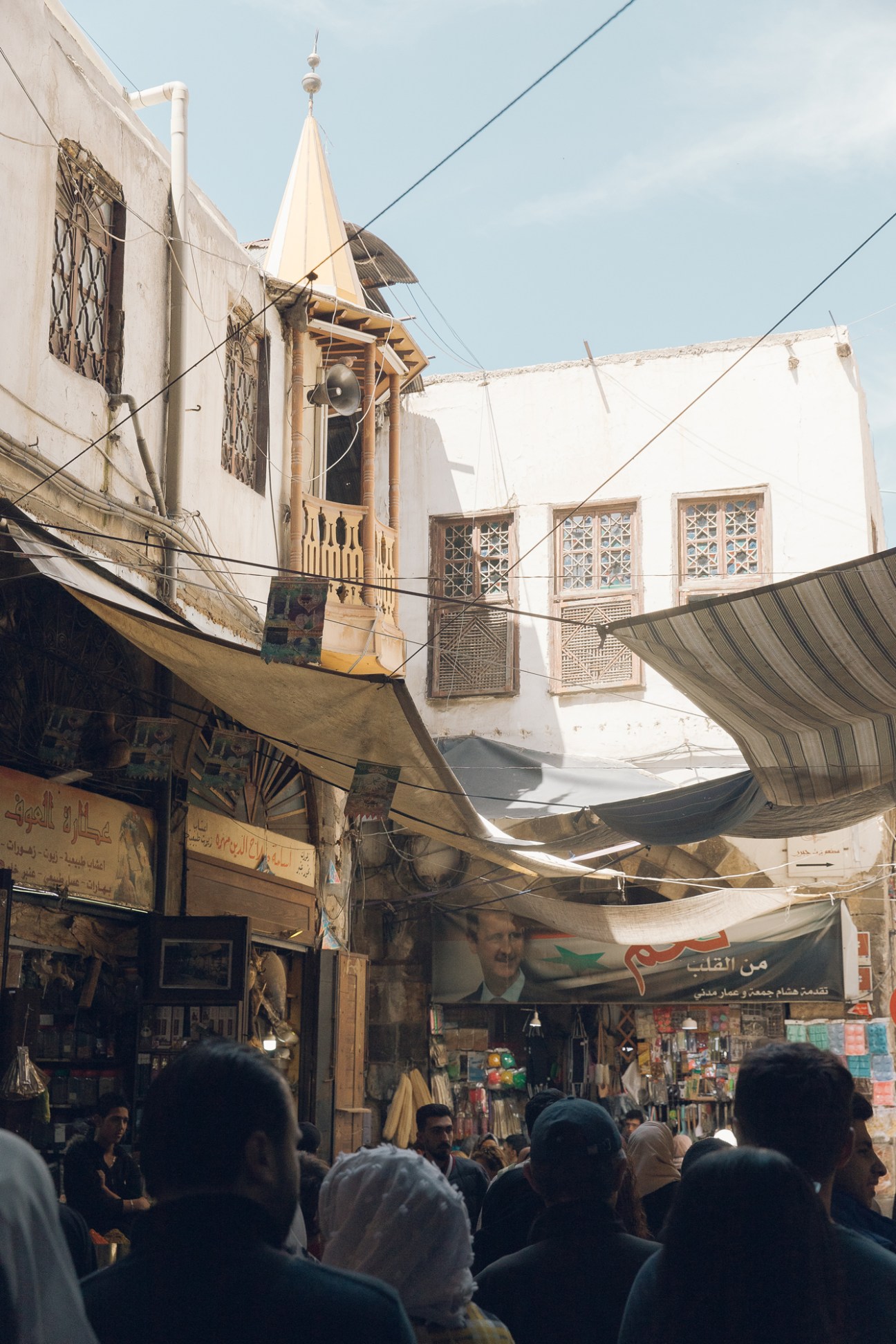 Crowded marketplace in Damascus's Old Town with traditional stone buildings, minaret, and people walking through narrow streets