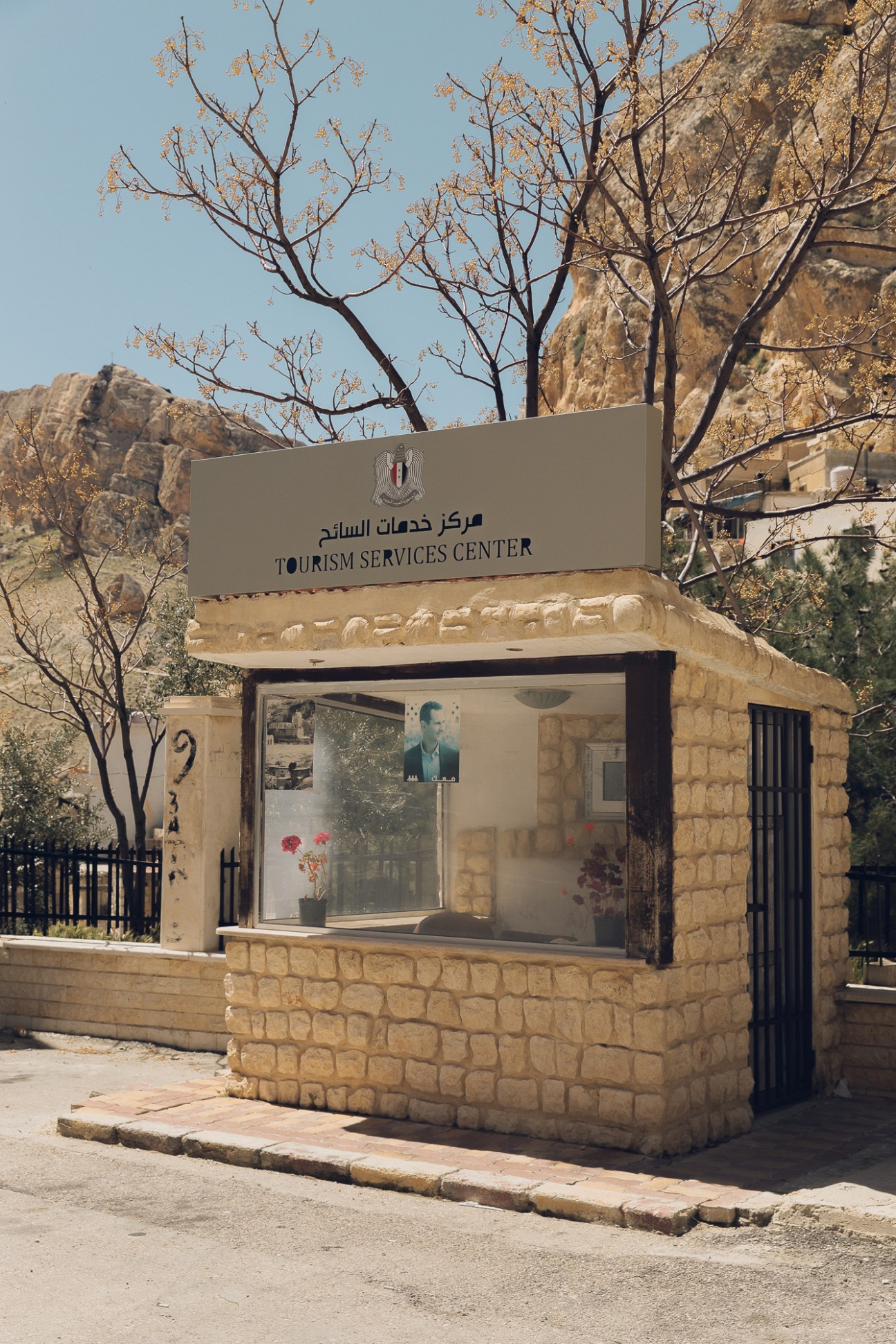 Small stone Tourism Services Center building with bilingual Arabic-English signage in a rocky mountainous landscape