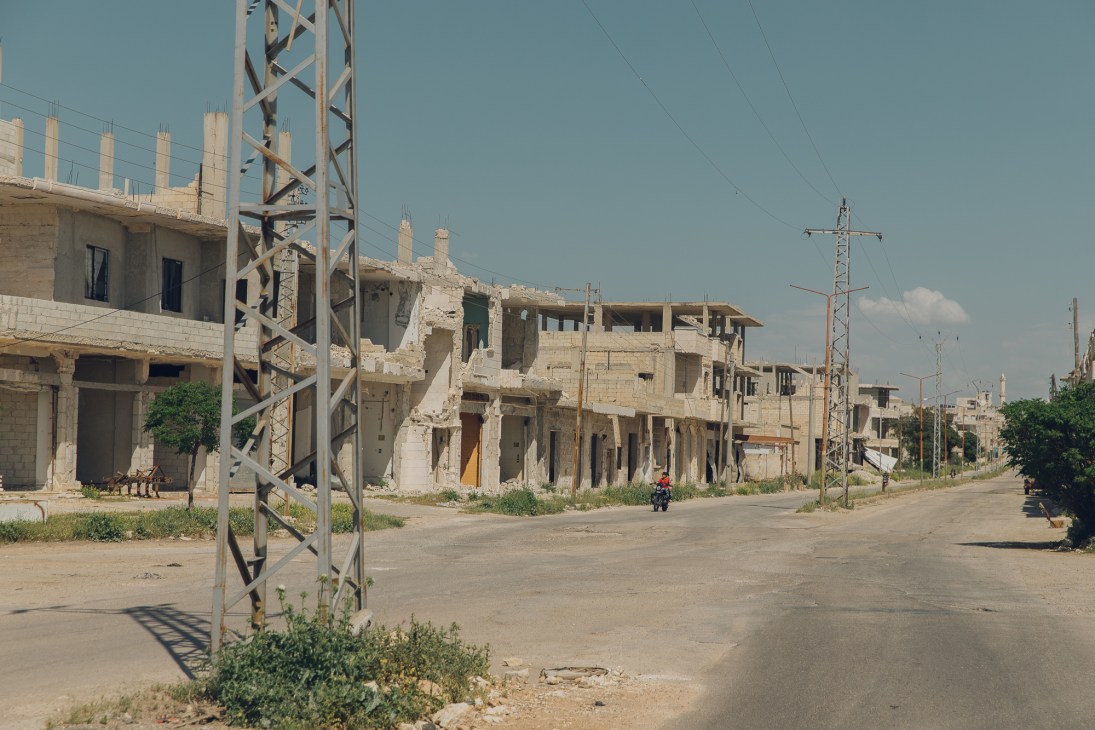War-damaged concrete buildings along a road with power lines and transmission tower
