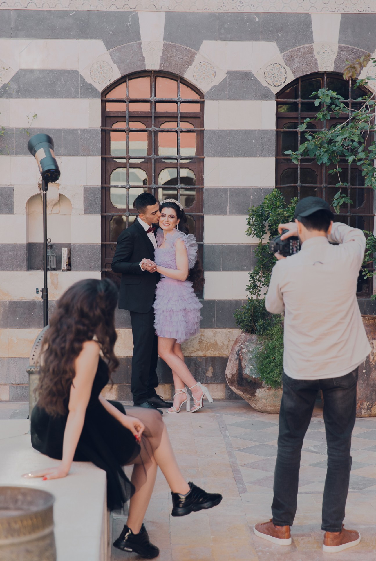 A couple posing for a photographer in formal attire against historic stone architecture