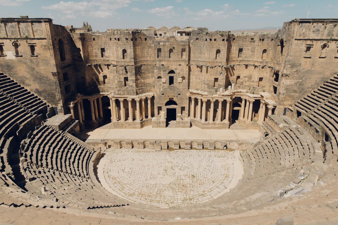 Ancient Roman amphitheatre ruins in Bosra showing circular stone seating and columned stage area