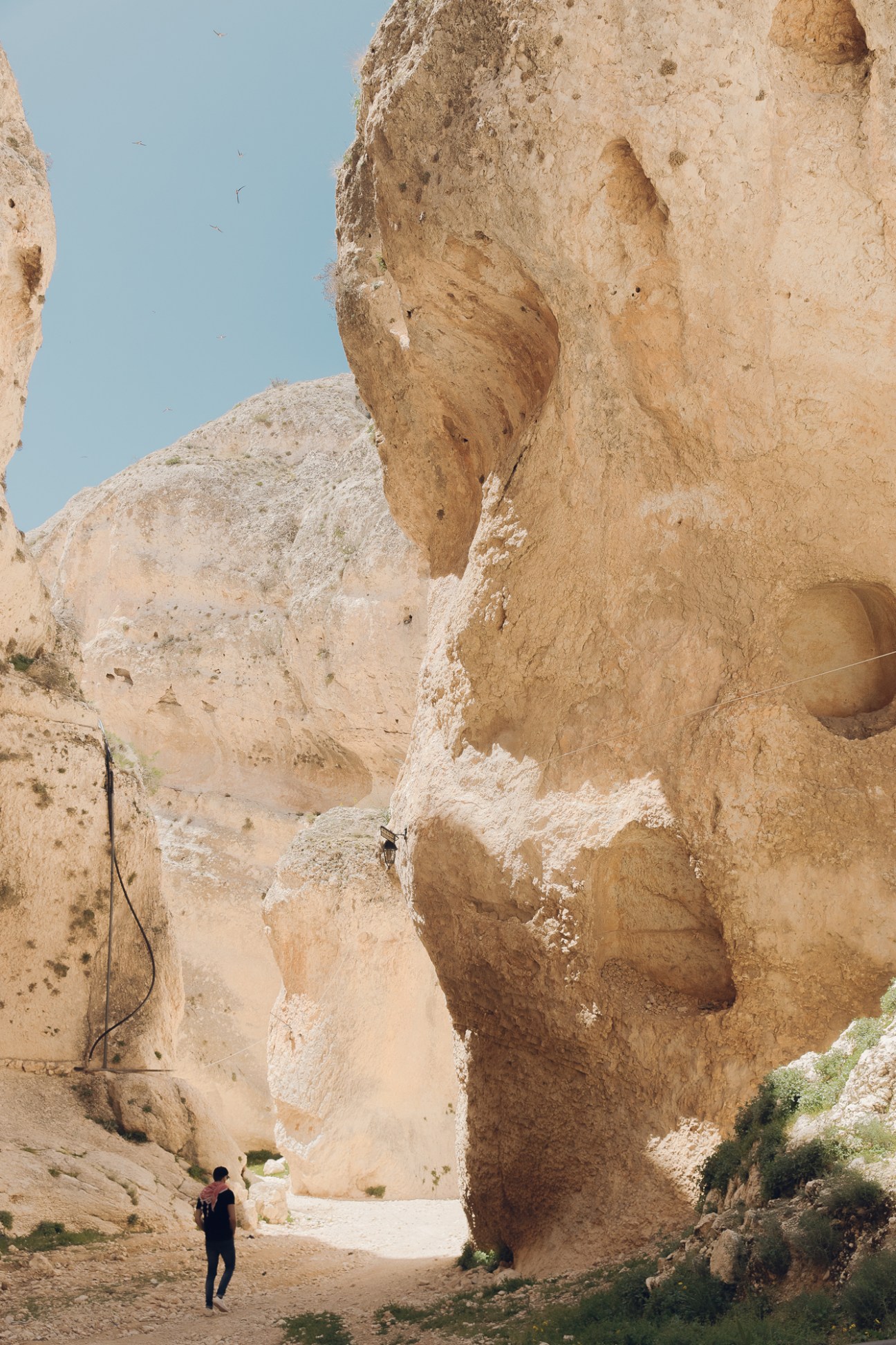 Tall limestone rock formations with carved cave openings and a person walking below for scale