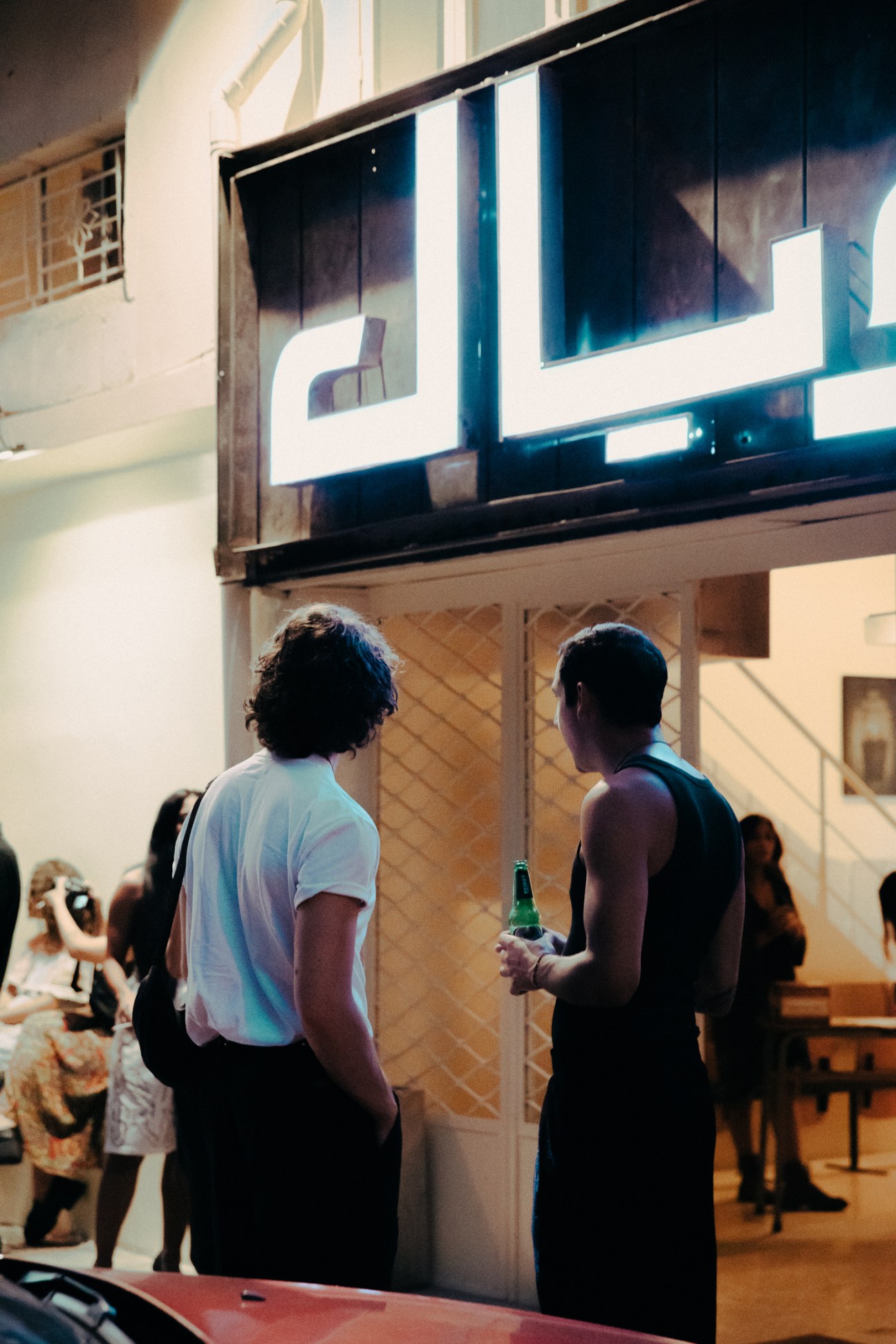 Two men watching a large screen in a modernist interior space with white walls and other visitors in background