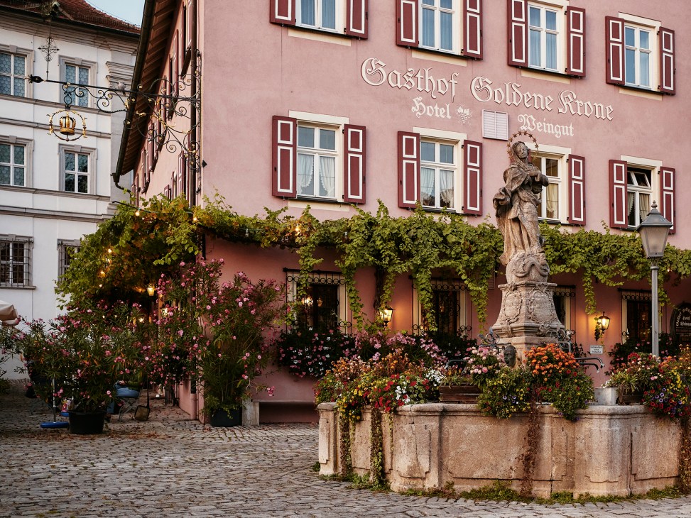 Pink historic hotel building with traditional shuttered windows and ornate statue in town square