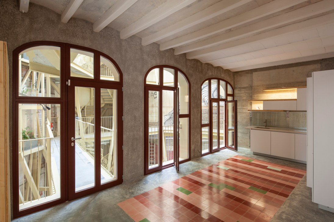 Modern apartment interior with exposed wooden ceiling beams, colorful tile flooring, and arched windows