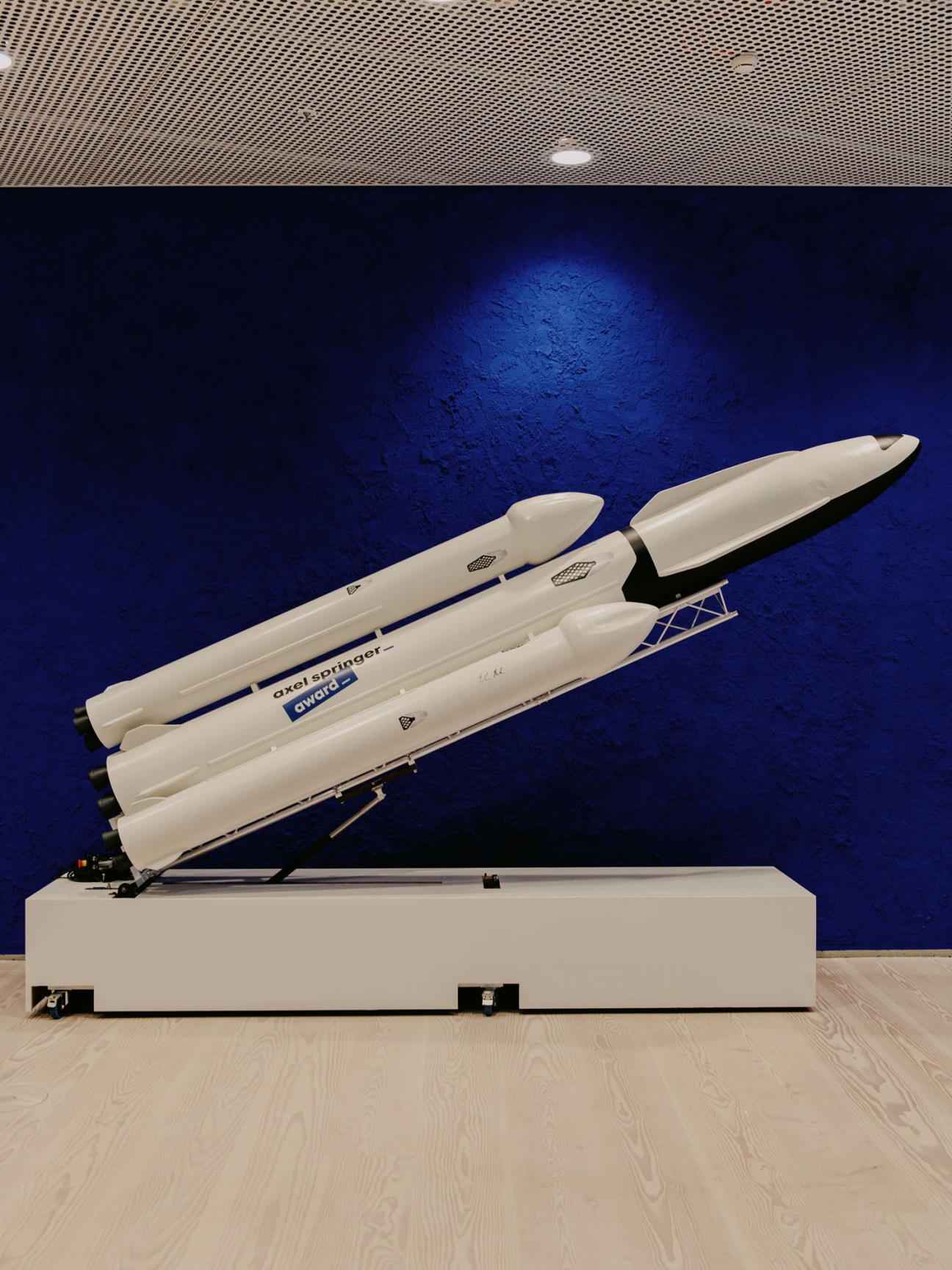 White model rocket on display stand with blue signature marking in modern office setting