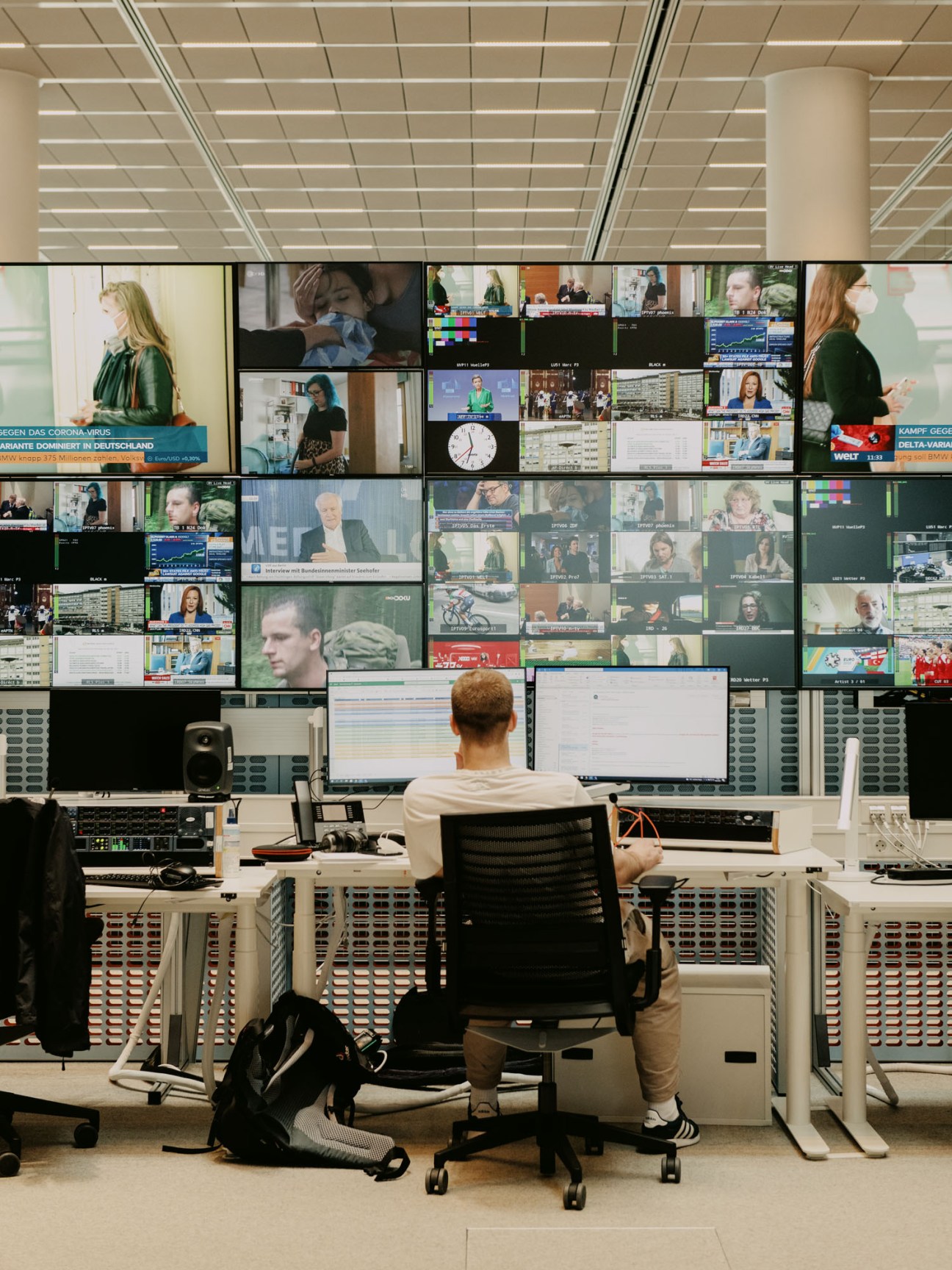 Person working at computer workstation surrounded by wall of multiple television monitors displaying news content
