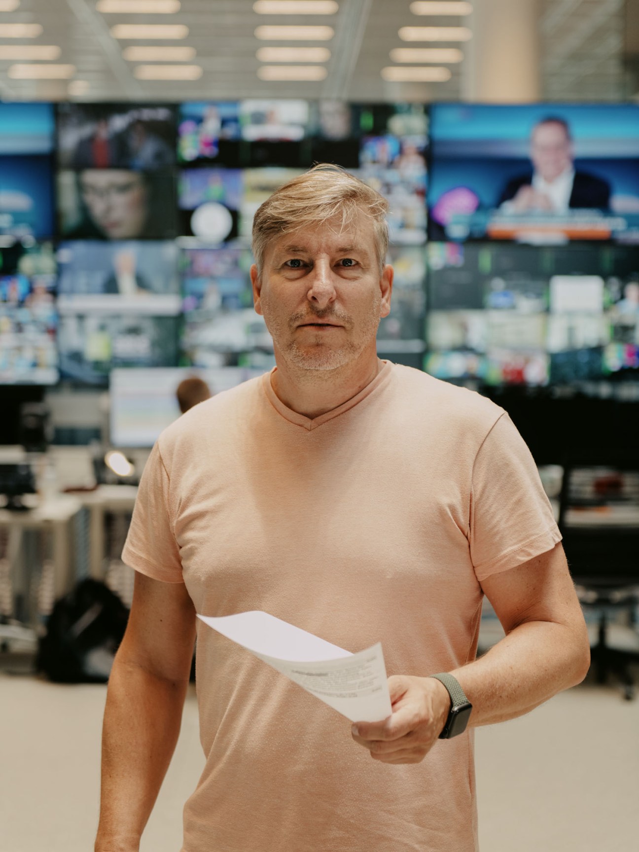 Oliver Münzberg, desk editor at Welt news channel, holding papers in newsroom with multiple monitors