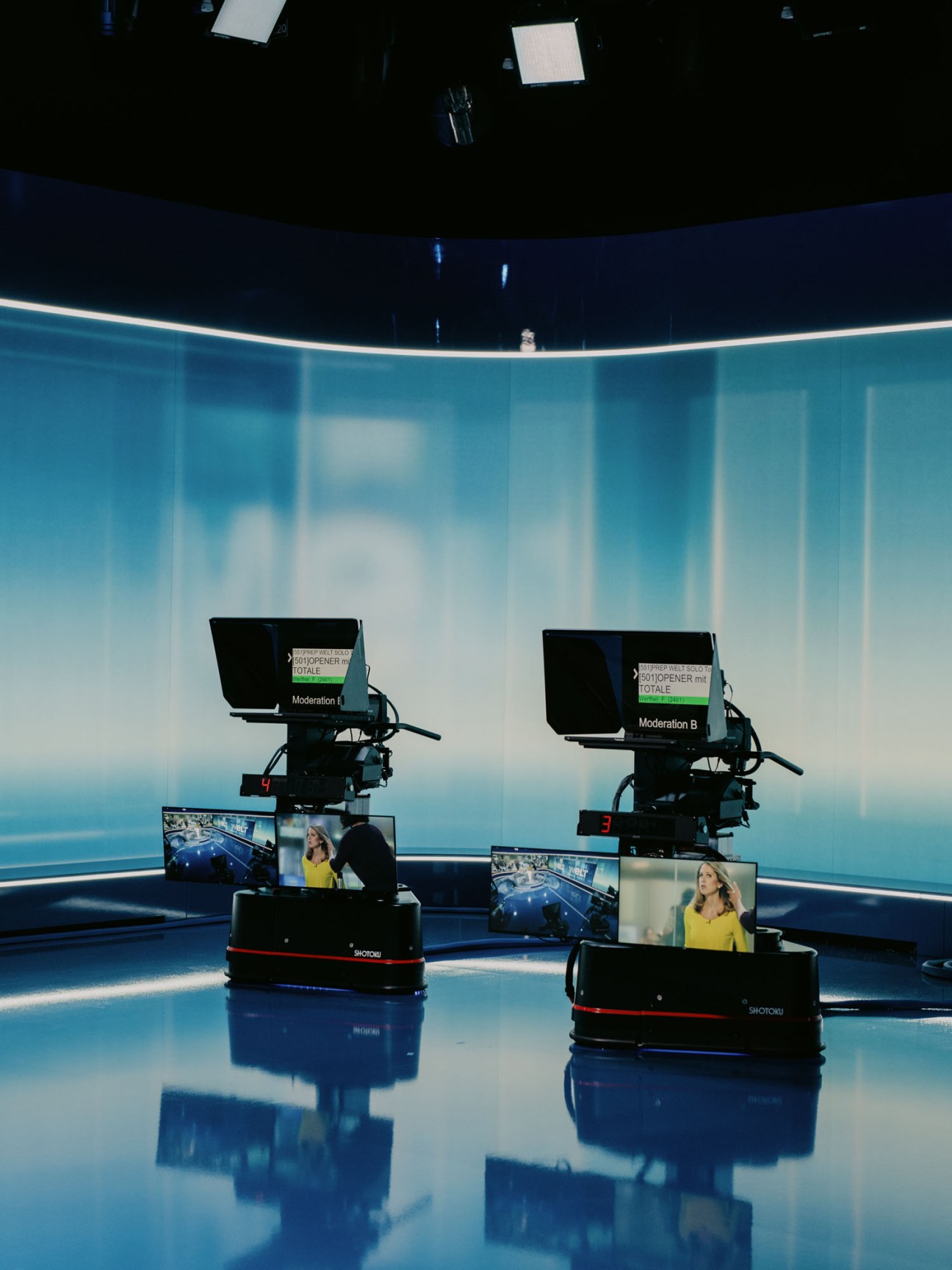 Professional television cameras mounted on robotic Shotoku bases positioned in blue-lit news studio