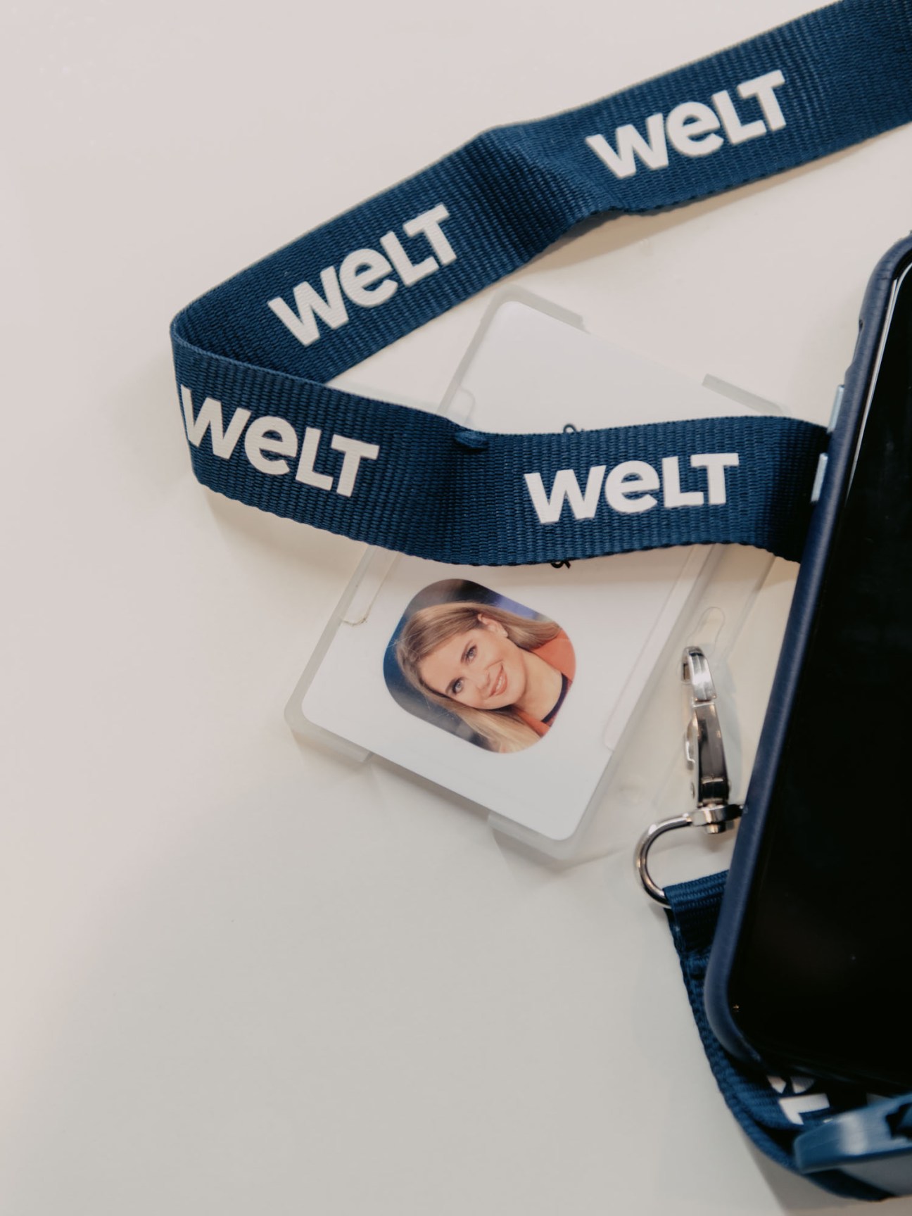Blue lanyard with 'WELT' branding attached to clear ID badge holder containing employee photo