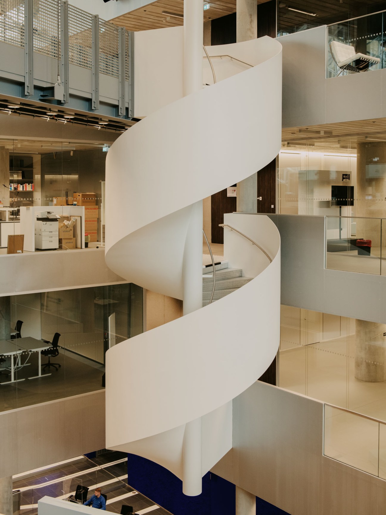 White spiral staircase with curved flowing design connecting multiple floors in modern office building