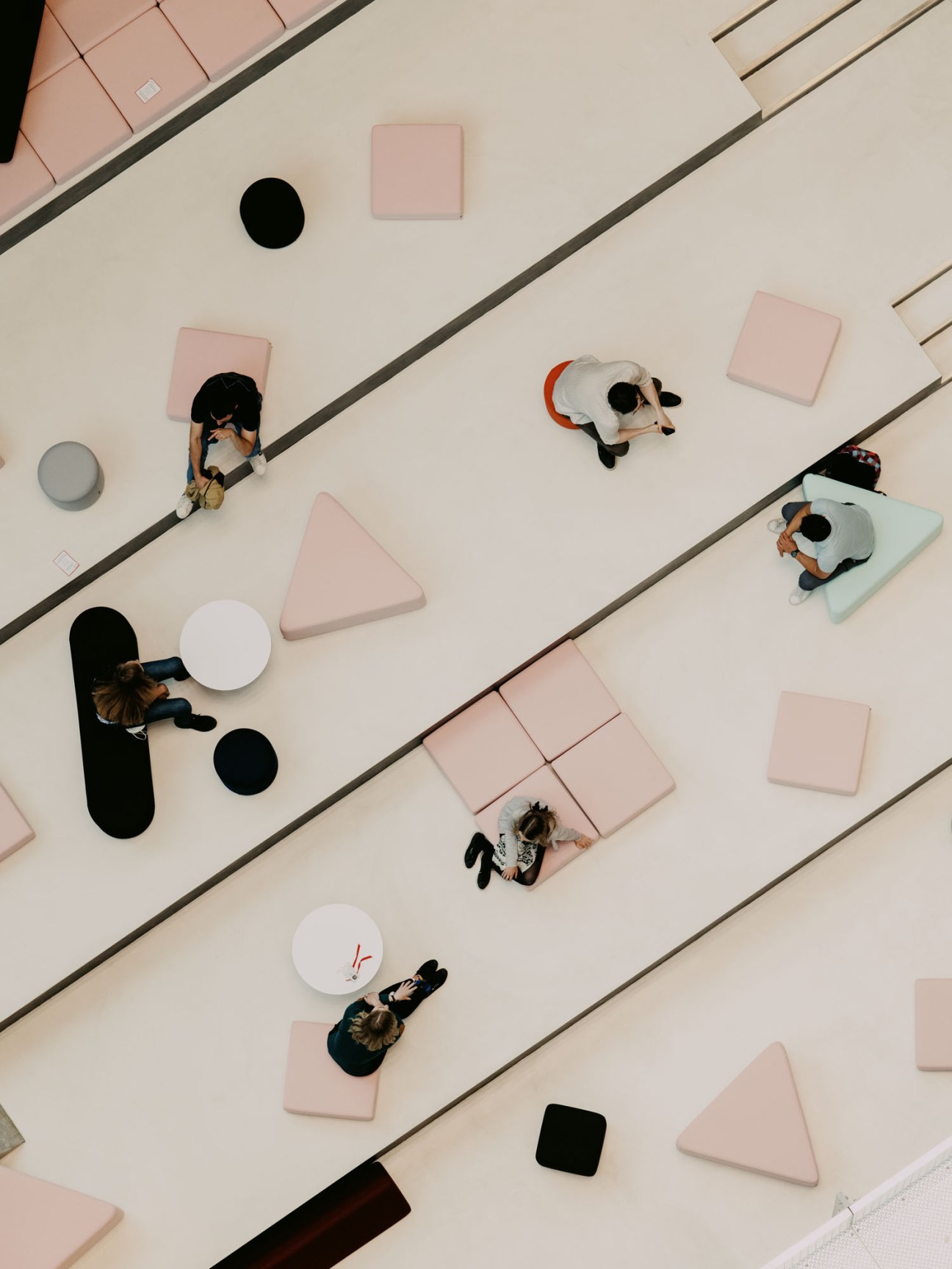 Aerial view of open office space with people working at geometric-shaped pink and white floor seating areas