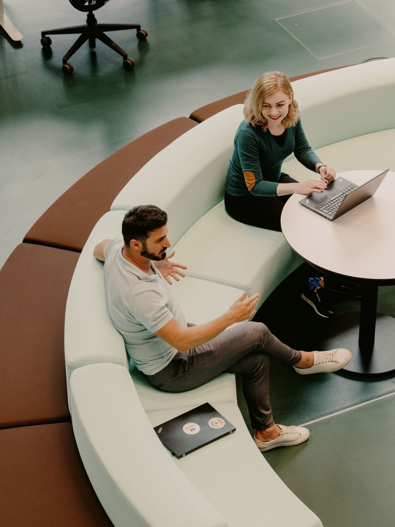 Woman sitting at modern curved workstation using laptop in contemporary office space with colleague nearby