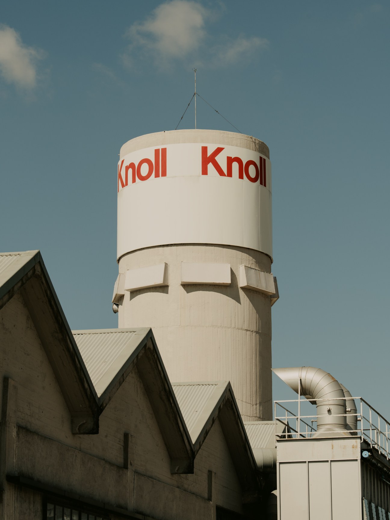 White cylindrical water tower with red Knoll logo text against blue sky with white clouds