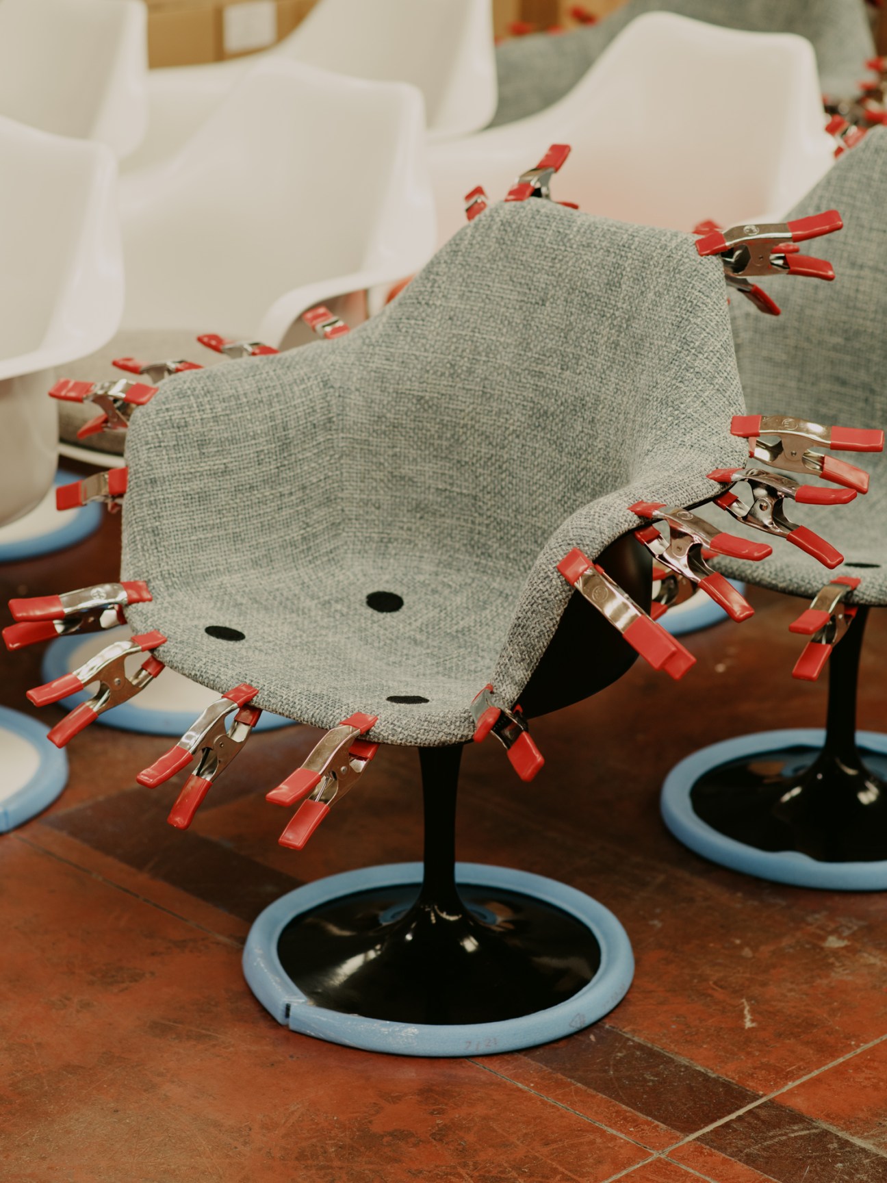 Gray upholstered chair with red clips attached around its edges during manufacturing process