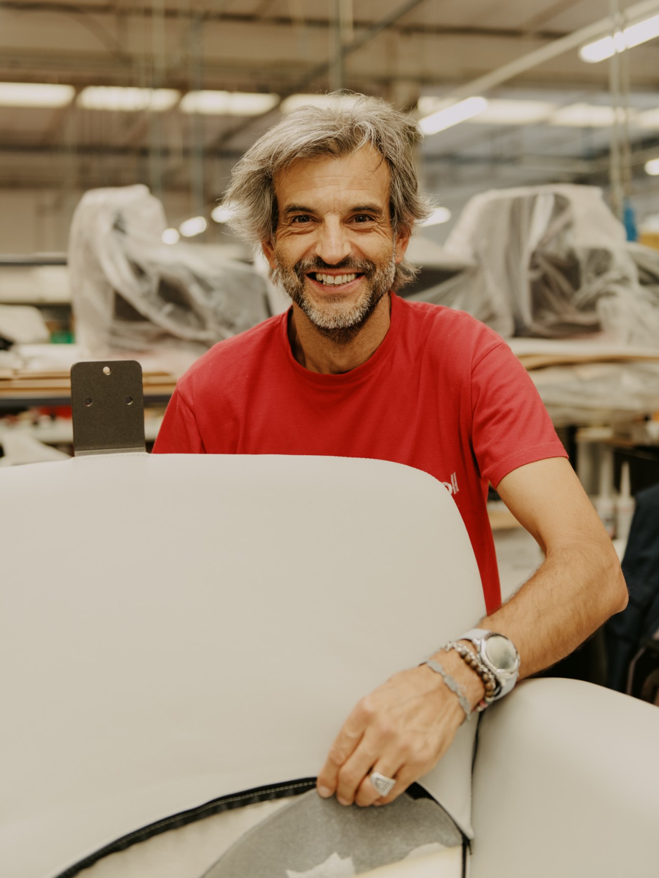 Piero Lissoni smiling in red shirt standing next to white curved furniture in factory workshop