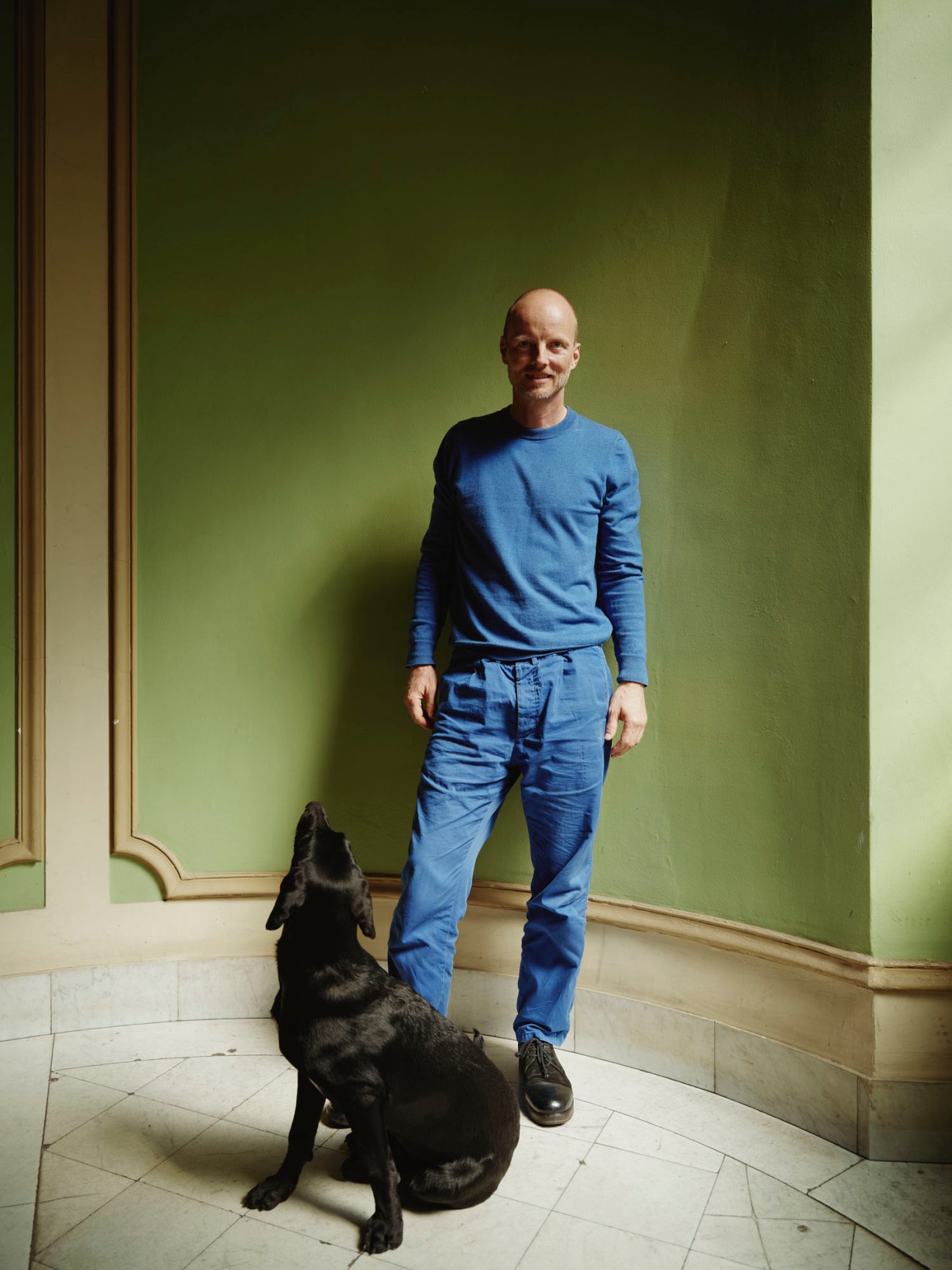 Thomas Kröger standing in an interior space with green walls and a black dog sitting beside him
