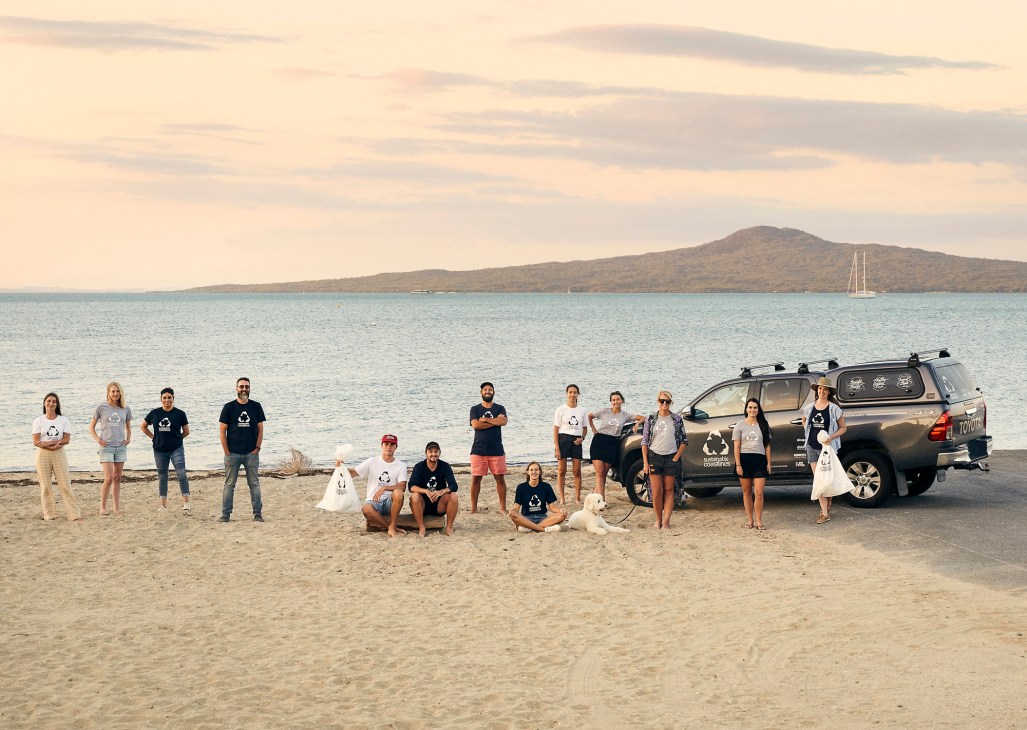 Sustainable Coastlines team members pose on a beach at sunset with bags of collected litter and a pickup truck