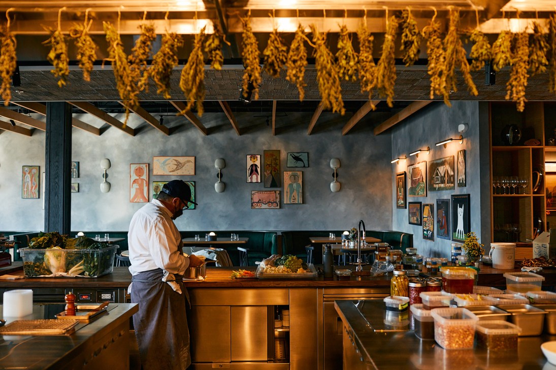 Chef working in restaurant kitchen with dried herbs hanging from ceiling and folk art on walls
