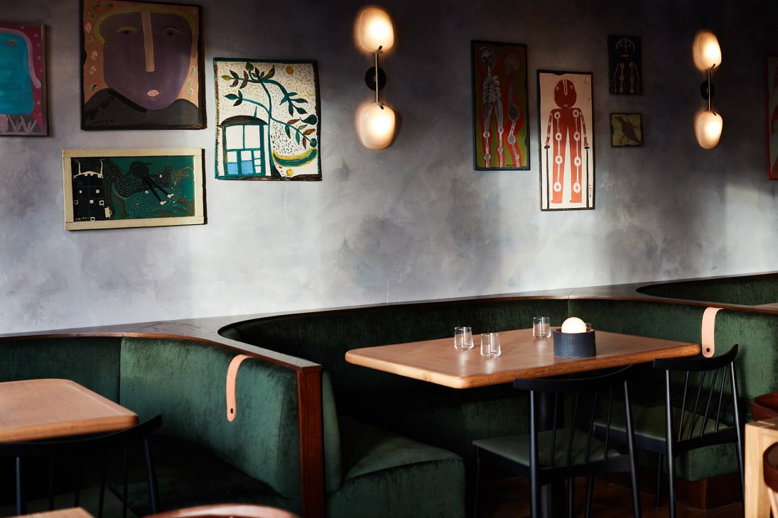 Restaurant interior at Audrey with green banquette seating, wooden tables, and folk art on gray walls