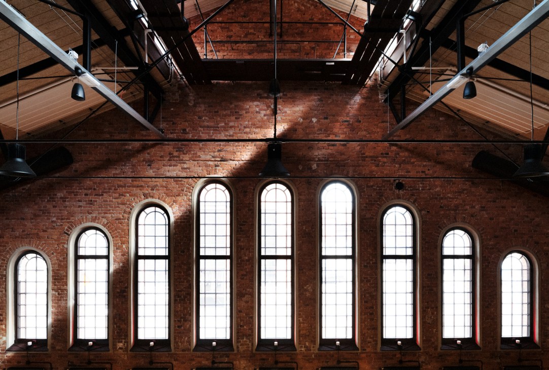 Renovated arched windows in the red brick wall of Berghs School's historic building with industrial ceiling details.