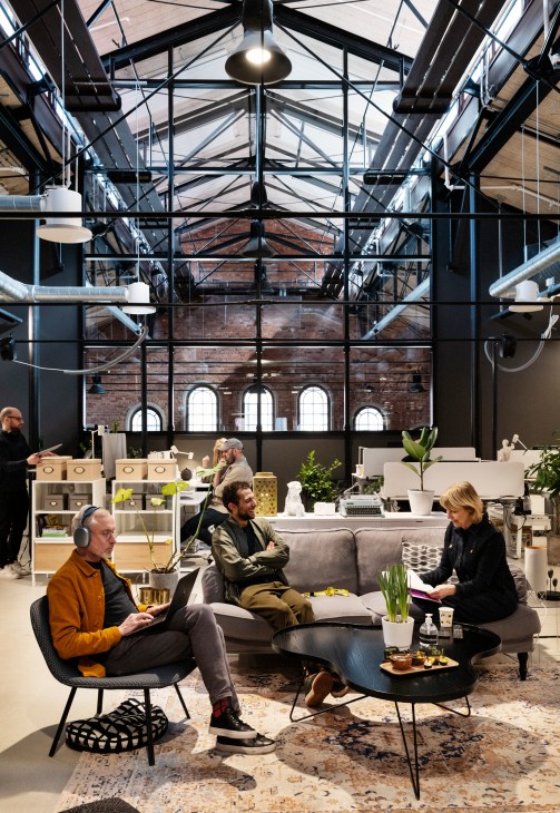 People meeting in a minimalist co-working space with industrial ceiling, arched windows, and modern furniture.